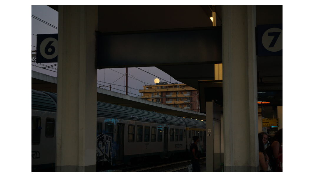 a photo of the full moon rising behind rain station platform roofs while waiting for the train.
