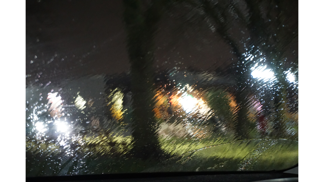 a view of houses windows lights heavily distorted by rain on the car windscreen.